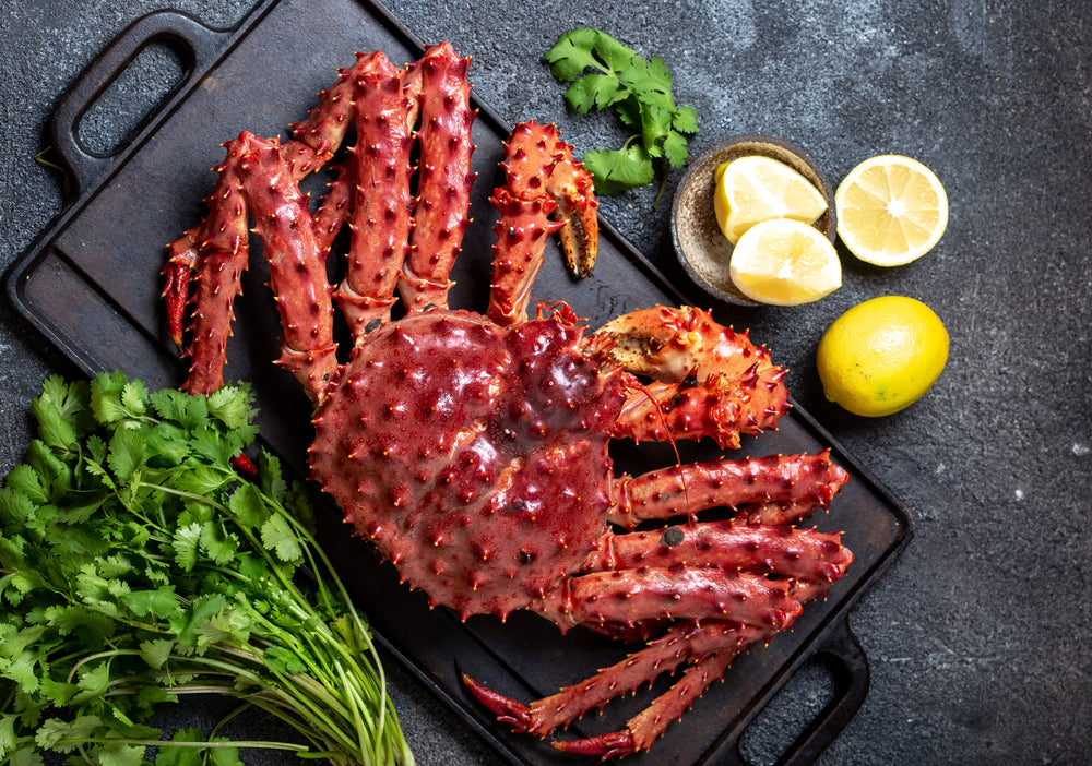 A king crab leg elegantly presented on a black background, garnished with lemon wedges and fresh cilantro.