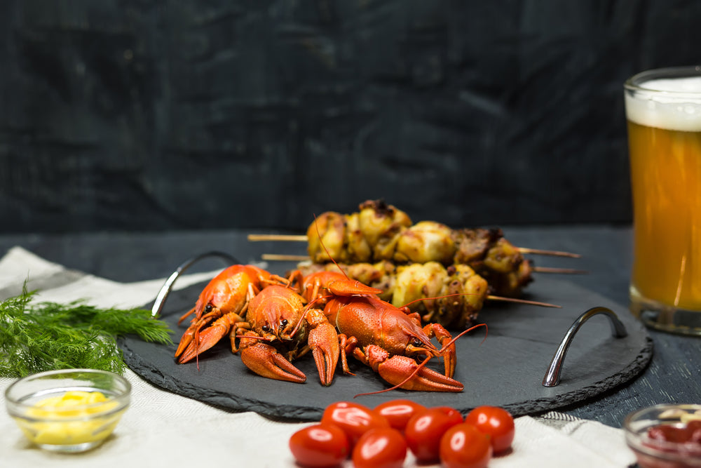 Tasty boiled crayfishes, barbecue and beer on wooden table with vegetables and sauce. 