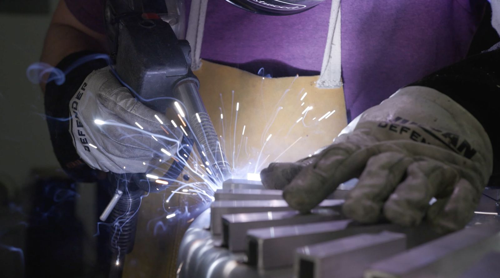 Gloved hands welding Tunnel Tubes onto a pot bottom, sparks flying